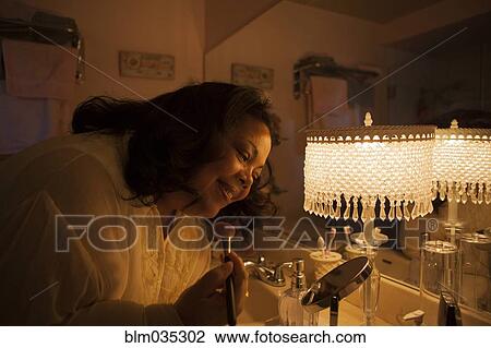 Stock Image - Woman applying makeup in bathroom mirror. Fotosearch