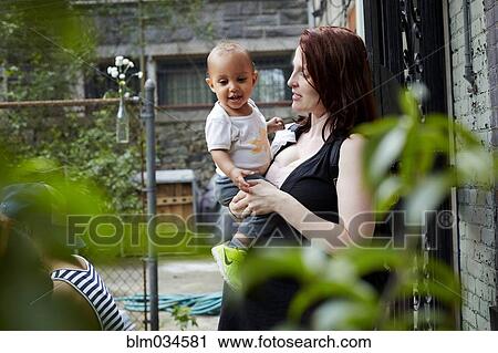 Stock Image - Woman holding baby son in backyard. Fotosearch