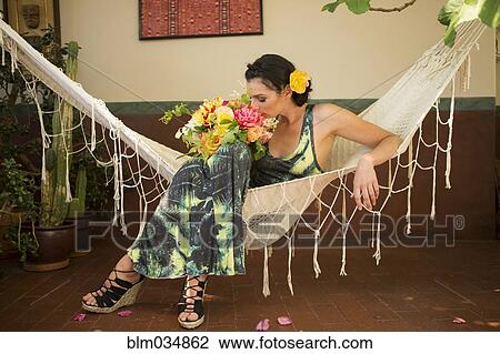 Stock Image - Woman smelling bouquet of flowers in hammock. Fotosearch