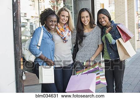 Stock Image - Women carrying shopping bags on city sidewalk. Fotosearch