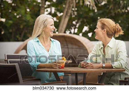 Stock Image - Women having cocktails on restaurant patio. Fotosearch