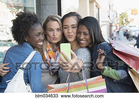 Stock Image - Women with shopping bags taking selfie in city. Fotosearch