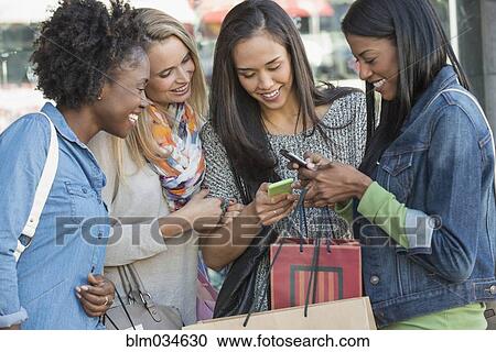 Stock Image - Women with shopping bags using cell phones. Fotosearch