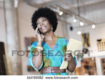 Stock Image - African American business owner talking on cell phone in store. Fotosearch