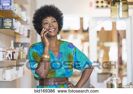 Stock Photograph - African American business owner talking on cell phone in store. Fotosearch