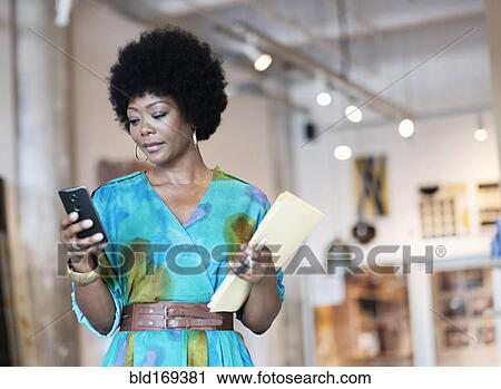 Stock Image - African American business owner using cell phone in store. Fotosearch