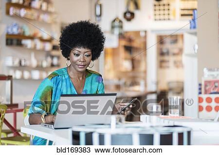 Stock Image - African American business owner using laptop in store. Fotosearch