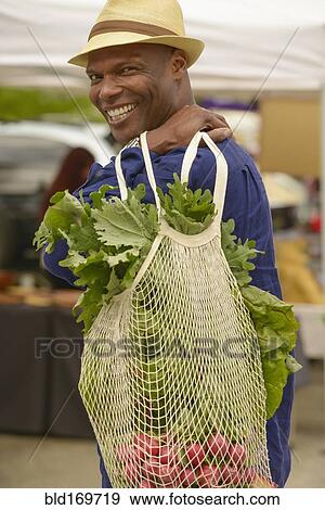 Stock Photo - African American man carrying bag of vegetables. Fotosearch