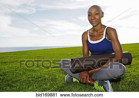 Stock Image - African American woman holding yoga mat in park. Fotosearch