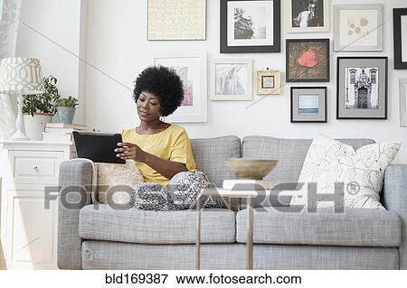 Stock Photo - African American woman using digital tablet on sofa. Fotosearch