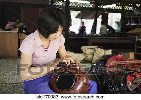 Stock Image - Asian artisan carving traditional design in workshop. Fotosearch