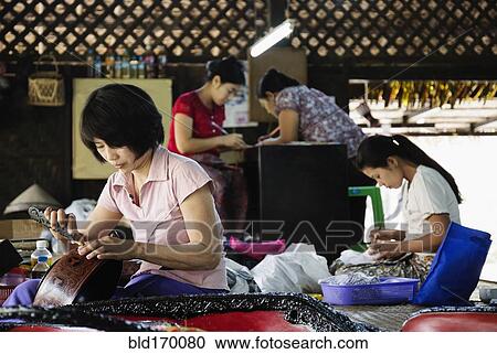 Stock Image - Asian artisans carving traditional designs in workshop. Fotosearch