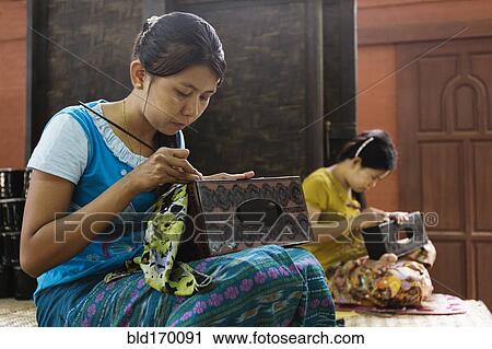 Stock Image - Asian artisans carving traditional design in workshop. Fotosearch