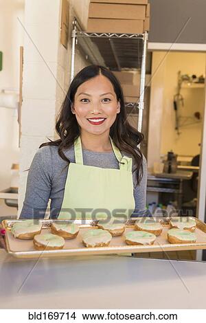 Picture - Asian baker holding tray of donuts in bakery. Fotosearch