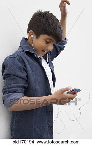 Picture - Asian boy listening to earbuds with cell phone. Fotosearch