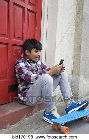 Stock Photo - Asian boy with skateboard using cell phone. Fotosearch