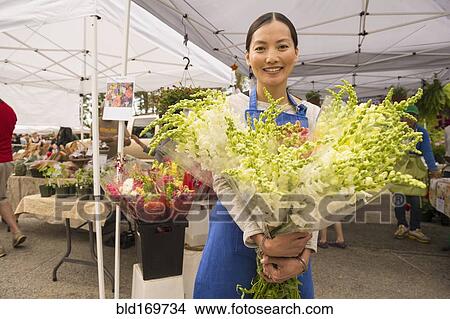 Picture - Asian clerk holding fresh flowers at farmers market. Fotosearch