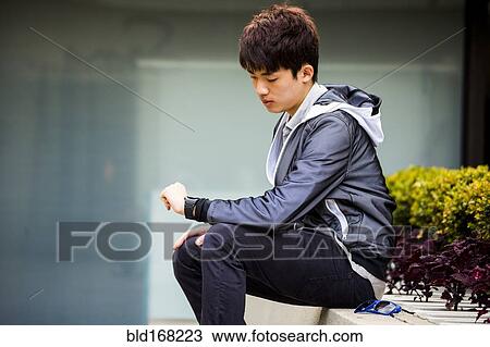 Stock Image - Asian man checking wristwatch in city. Fotosearch
