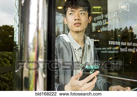 Stock Image - Asian man holding cell phone in doorway. Fotosearch
