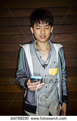 Stock Image - Asian man listening to music with cell phone. Fotosearch