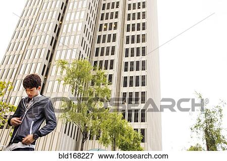 Asian man standing near urban skyscraper View Large Photo Image Stock Photo - Asian man standing near urban skyscraper. Fotosearch