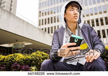 Stock Photograph - Asian man using cell phone in city. Fotosearch