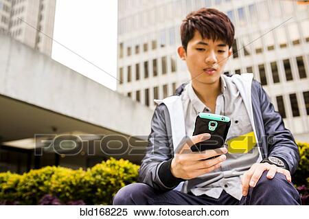 Stock Photography - Asian man using cell phone in city. Fotosearch