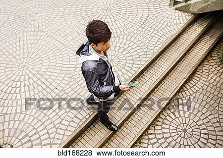 Stock Photo - Asian man using cell phone in courtyard. Fotosearch