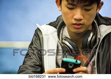 Stock Image - Asian man with headphone using cell phone. Fotosearch