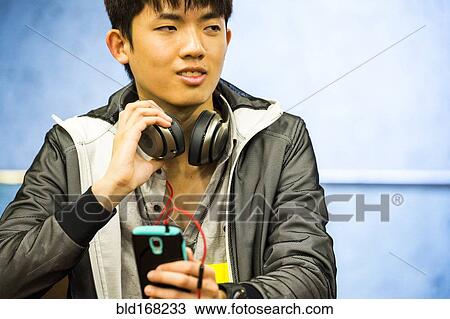Stock Image - Asian man with headphone using cell phone. Fotosearch