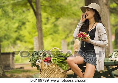 Stock Photo - Asian woman talking on cell phone on picnic table. Fotosearch