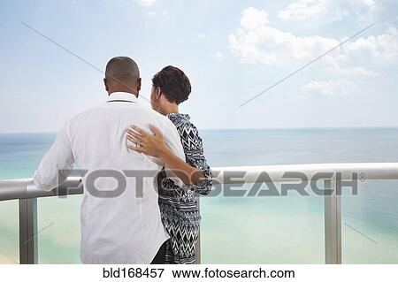 Stock Photo - Black couple hugging on balcony over ocean. Fotosearch