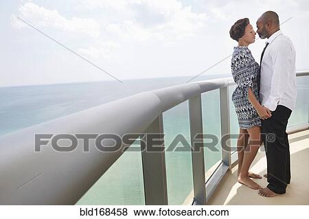 Stock Photo - Black couple kissing on balcony over ocean. Fotosearch