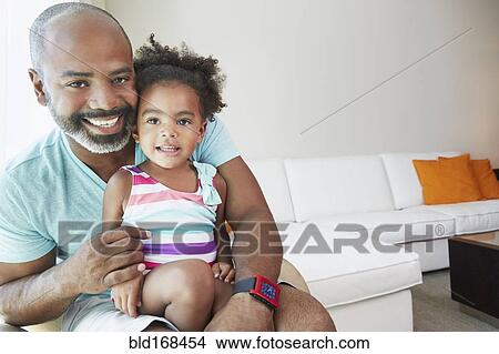 Picture - Black father and daughter sitting in living room. Fotosearch