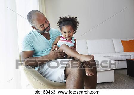 Stock Image - Black father and daughter sitting in living room. Fotosearch