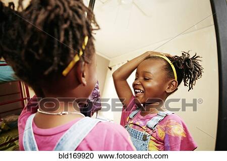 Stock Image - Black girl admiring herself in mirror. Fotosearch