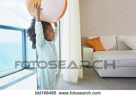 Stock Photograph - Black girl playing with beach ball in living room. Fotosearch