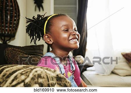 Stock Image - Black girl smiling on sofa. Fotosearch