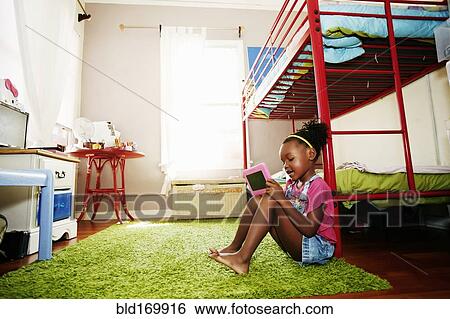 Stock Photograph - Black girl using digital tablet in bedroom. Fotosearch