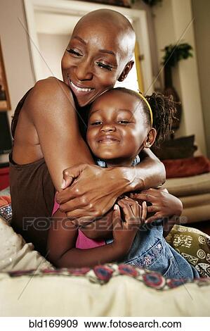 Stock Photo - Black mother and daughter hugging on sofa. Fotosearch