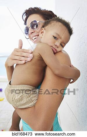 Stock Image - Black mother applying sunscreen to son at beach. Fotosearch