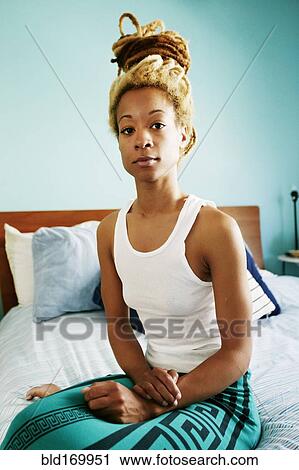 Stock Image - Black woman sitting on bed. Fotosearch