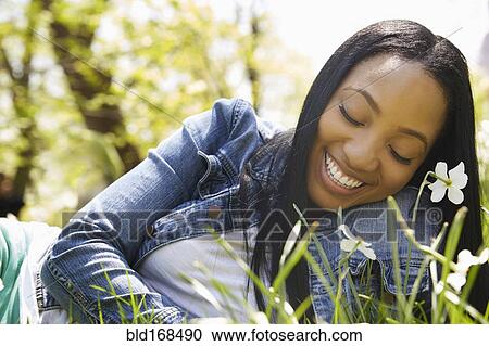 Stock Image - Black woman smiling in grass in park. Fotosearch