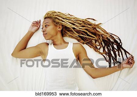 Stock Image - Black woman with dreadlocks laying on bed. Fotosearch