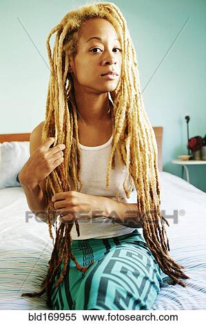 Stock Photography - Black woman with dreadlocks sitting on bed. Fotosearch