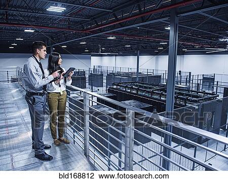 Stock Image - Business people examining server room from balcony. Fotosearch