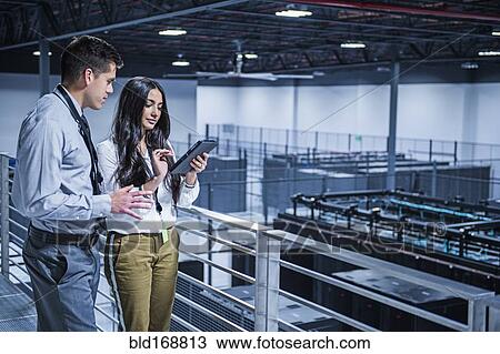 Stock Image - Business people using digital tablet over server room. Fotosearch