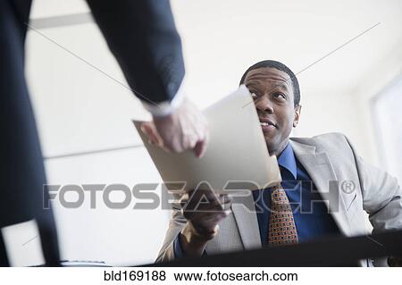 Stock Photo - Businessman handing folder to boss in office. Fotosearch