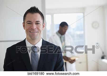 Stock Image - Businessman smiling in office with doctor. Fotosearch