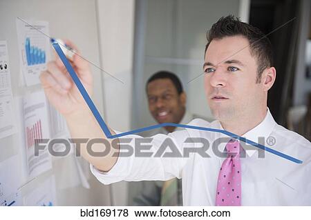 Stock Photo - Businessman writing graph on glass wall in office. Fotosearch